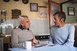 © Halfpoint - Portrait of man with elderly father sitting at the table indoors at home, talking.