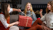 © ako-photography - three young girls sitting on the couch and having fun unwrapping Christmas presents at home