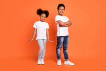 Full Length Photo Of Little Cool Girl Boy Crossed Arms Wear White T-shirt Jeans Sneakers Isolated On Orange Background