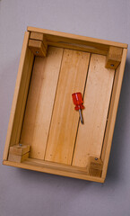 brown wooden box on a white background with a red phillips screwdriver background texture.the screwdriver is lying on a wooden box. the twisted screw is handmade. the box is handmade. wooden box with