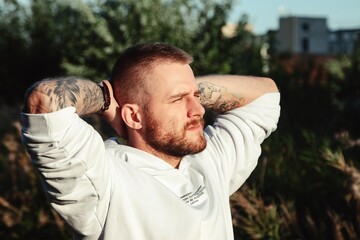 Wall Mural - Portrait of young bearded man with tattoos in white jacket in countryside