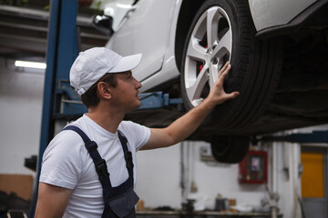 Wall Mural - Male car service worker examining wheels of a car on the lift