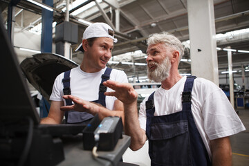 Wall Mural - Elderly mechanic talking to his colleague while doing computer car diagnostics