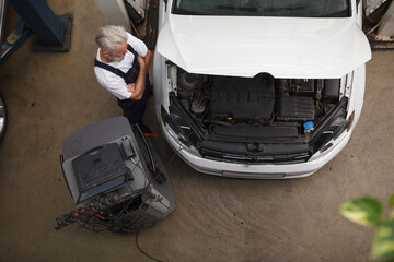 Wall Mural - Top view shot of an experienced car service worker examining car under the hood