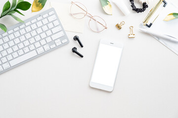 Minimal home office desk table with smartphone mockup, computer keyboard, glasses, clipboard on white background. Flat lay, top view, copy space. Business, technology concept.