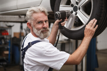 Wall Mural - Senior bearded car mechanic smiling to the camera while working with torque wrench at the garage