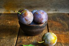 Home Harvest Fresh Plums In A Ceramic Bowl On A Wooden Table.