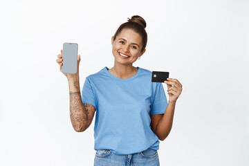 Beautiful young woman showing empty phone screen with credit card, app interface, smiling at camera, white background
