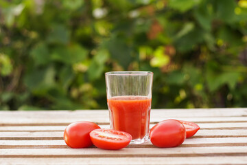 Glass of red tomato juice with vegetables on wooden table