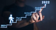 © Miha Creative - Businessman pointing to the growing plan of successful business in 2022 year and a figure climbs the ladder of success. Year 2022 plan, action and goals.
