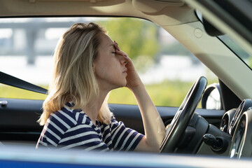 Upset or tired female driver rubbing nose and forehead sitting inside car driving. Middle aged woman suffering from headache, migraineee, panic attack or pms syndrome in vehicle in traffic jam on road