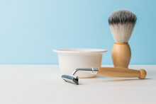 A Ceramic Bowl, A Shaving Brush And A Razor With A Wooden Handle On A White Table. Space For The Text.