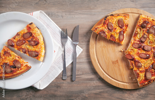 Slice of pizza on plate, fork, knife on wooden table. Pizza on circle board