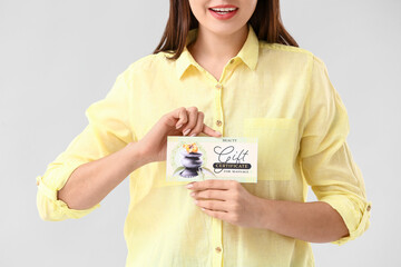 Poster - Young woman with gift certificate for massage on light background