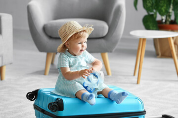 Cute baby girl with suitcase at home