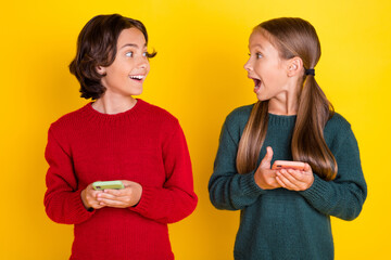 Poster - Photo portrait two children amazed using cellphones looking each at other isolated vivid yellow color background