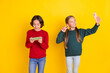© deagreez - Photo portrait girl taking selfie showing v-sign boy playing video game on cellphone isolated vibrant yellow color background
