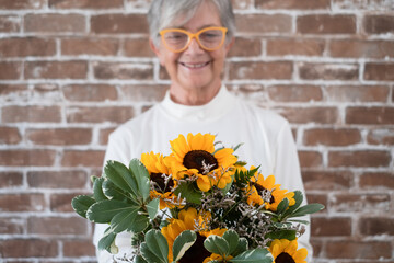 Wall Mural - Beautiful bouquet of sunflowers in hand of smiling senior woman - brick wall background