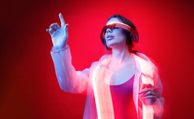 Woman in futuristic costume. Girl in glasses of virtual reality while touching air. Augmented reality game, future technology, AI concept. VR. Neon red light.