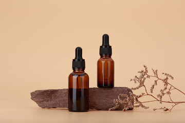 Two skin serum bottles next to natural stone and dry flower against beige  background with copy space. Concept of luxury skin serum for anti aging treatment