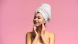 joyful woman with towel on head applying face mask while looking away isolated on pink