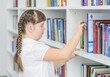 Young girl with syndrome down chooses books in the library. Education for disabled children concept
