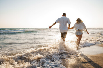 Wall Mural - Young beautiful couple walking on beach near sea