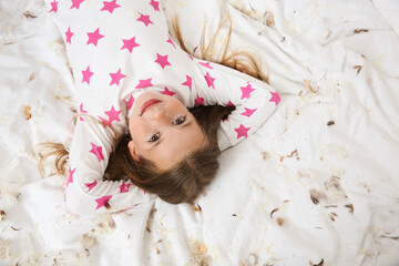 Wall Mural - Cute little girl in pajamas lying among feathers on bed, top view. Happy childhood