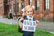 © Victor - Portrait of a schoolgirl with a sign in her hands with the words Back to school. Against the background of an old building.