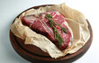 Raw porterhouse steak with rosemary. Beef steak with parchment on a wooden board on a white table. Background image, copy space
