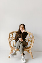 Studio Shot Of Young Woman Sitting In Wicker Chair