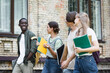 © LIGHTFIELD STUDIOS - African american student with laptop walking near friends outdoors