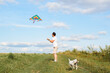 © Sergio - Man launches rainbow colored kite into blue sky, plays with his dog in field outdoors, jack russell terrier runs with stick in his teeth. Selective focus on man in casual clothes standing on meadow