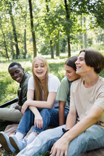 Cheerful Teen Friends Sitting Near African American Boy With Acoustic Guitar In Park