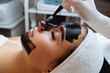 © руслан малыш - cosmetologist applying black mask on pretty woman face wearing black gloves, gorgeous woman in spa having facial procedures