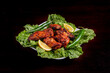Tandoori Barbeque chicken wings on a bed of lettuce on a dark table