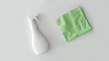 Green rubber spray bottle with chemical detergent and green rag wiping up white table background.