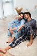 positive young gay couple sitting on carpet near bed