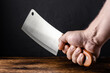 © Konstiantyn Zapylaie - Male hand holds a large meat knife on a wooden background.