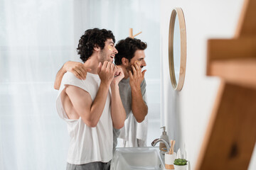 happy gay couple applying eye patches in bathroom