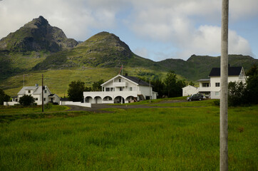 Wall Mural - White buildings in the green field below the hills against a cloudy sky