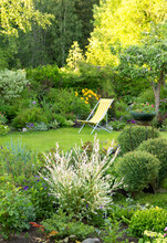 Beautiful Flower Garden With Green Lawn And Yellow Garden Chair On It In Summer, Vertical (sharpness At The Leading Edge Of The Frame)
