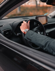 Poster - Closeup view of a man wearing the suit and a watch and driving a car on a blurry background