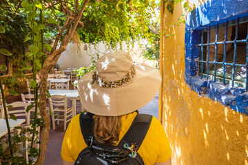 Aufkleber - A young tourist wearing a hat and a small backpack is walking along the picturesque street