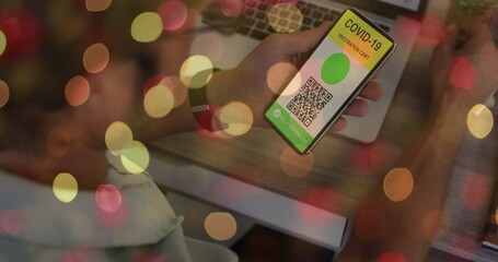 Poster - Animation of man holding smartphone with covid 19 vaccination passport over blurred lights