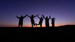 Beautiful shot of the silhouettes of five children jumping and holding hands during sunset