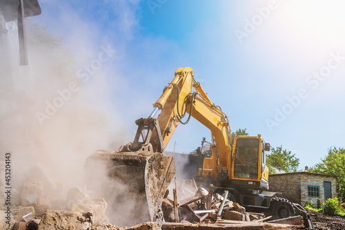 Excavator breaks old house, many dust in air. Building demolition and deconstruction, copy space.