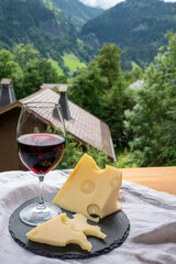 Cheese collection, French cow cheese emmental, glass of red wine from Savoie and french mountains village in Haute-Savoie on background