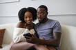 © Creative Flame - Smiling couple sitting on sofa and using smart phone