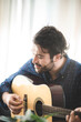 © chokniti - Handsome young man relaxing and enjoying playing guitar with eyes closed at home while feeling every rhythm